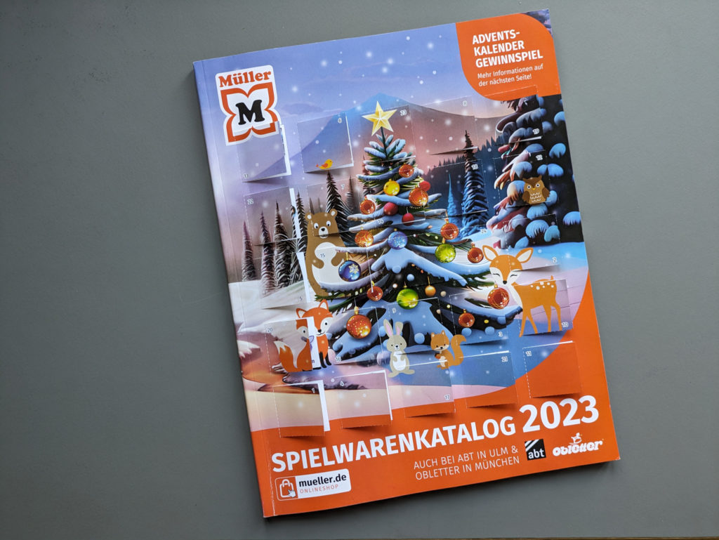 Foto des Müller Spielwarenkatalogs 2023. Auf der Titelseite sind die geöffneten Papiertürchen des Adventskalendergewinspiels.